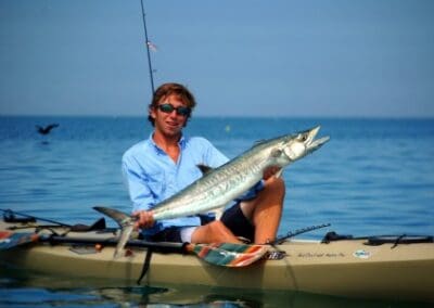 Man holding fish on kayak in ocean.