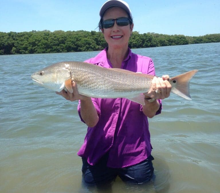 Person holding fish in water, smiling.