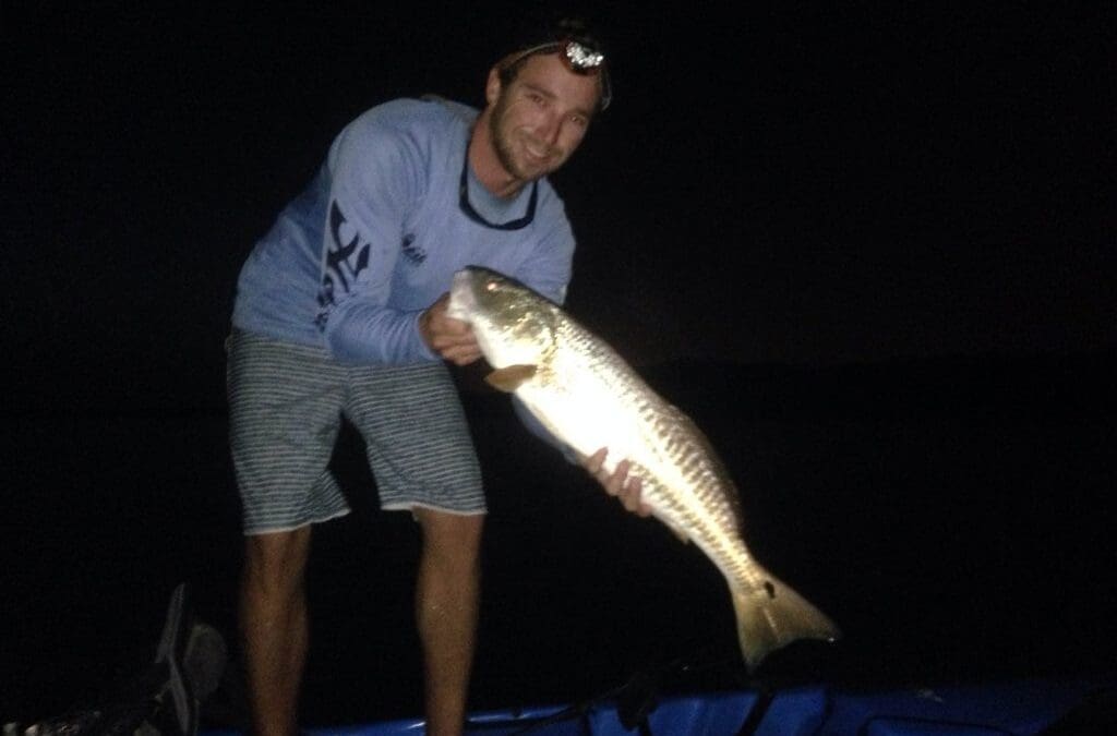 Person proudly holding large fish at night.