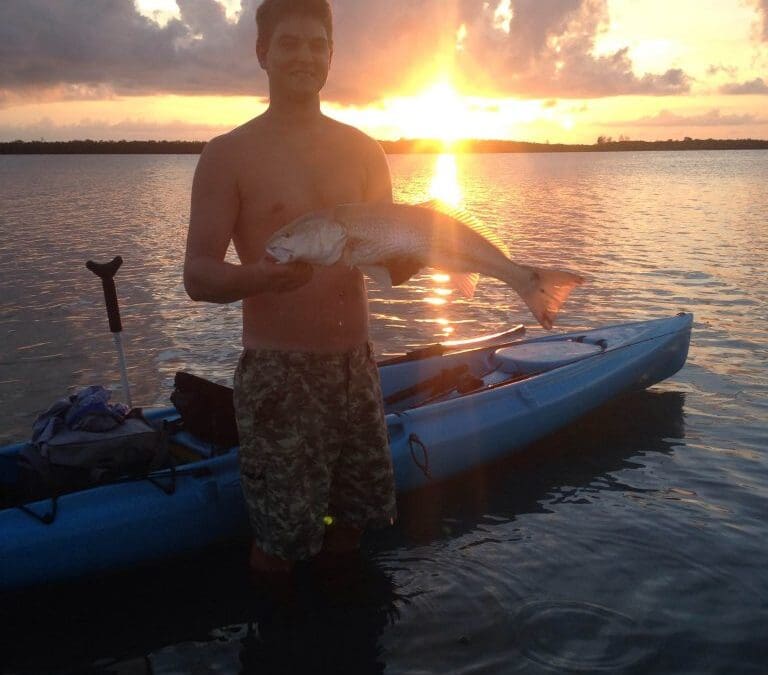 Man holding fish at sunset by kayak