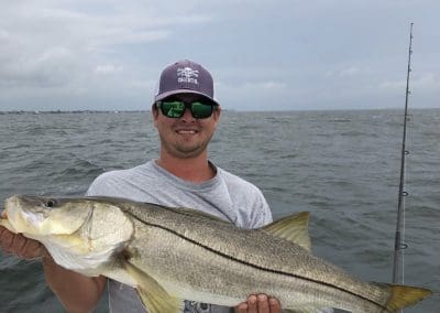 man holding a snook fish while on a inshore